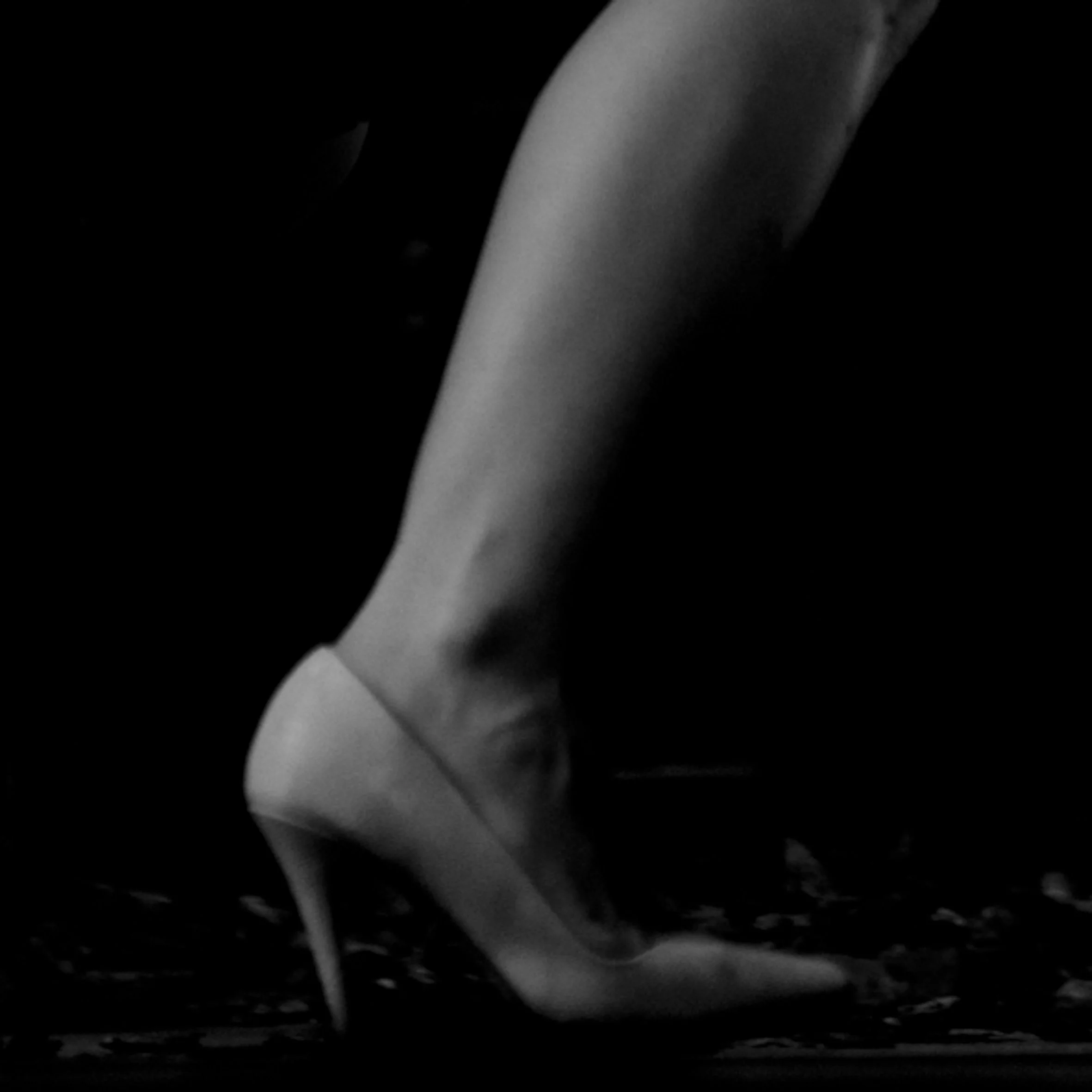 Une jambe portant une chaussure à talon haut dans un décor sombre.