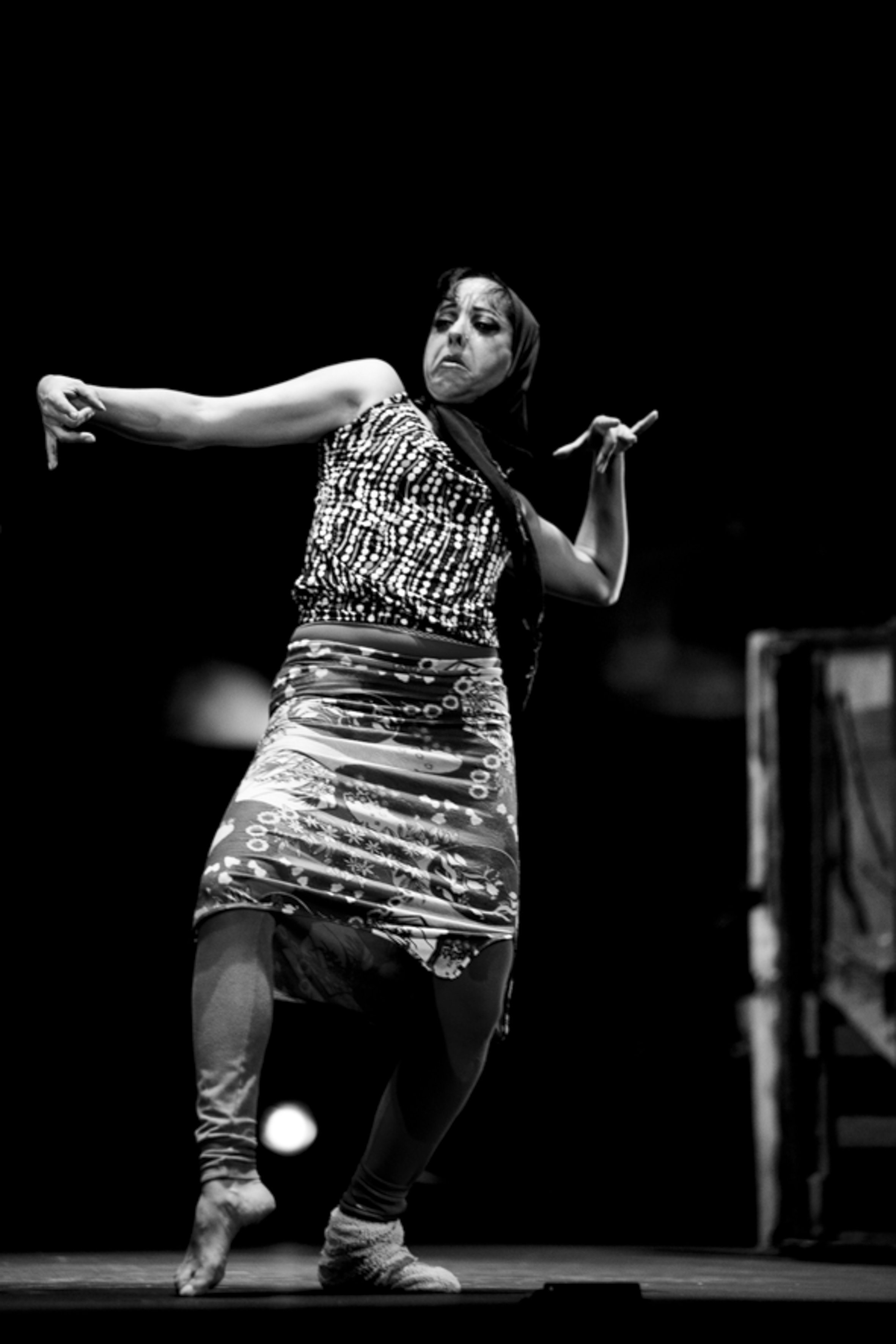 Une femme danse sur scène dans une performance expressive, avec une expression faciale dramatique.