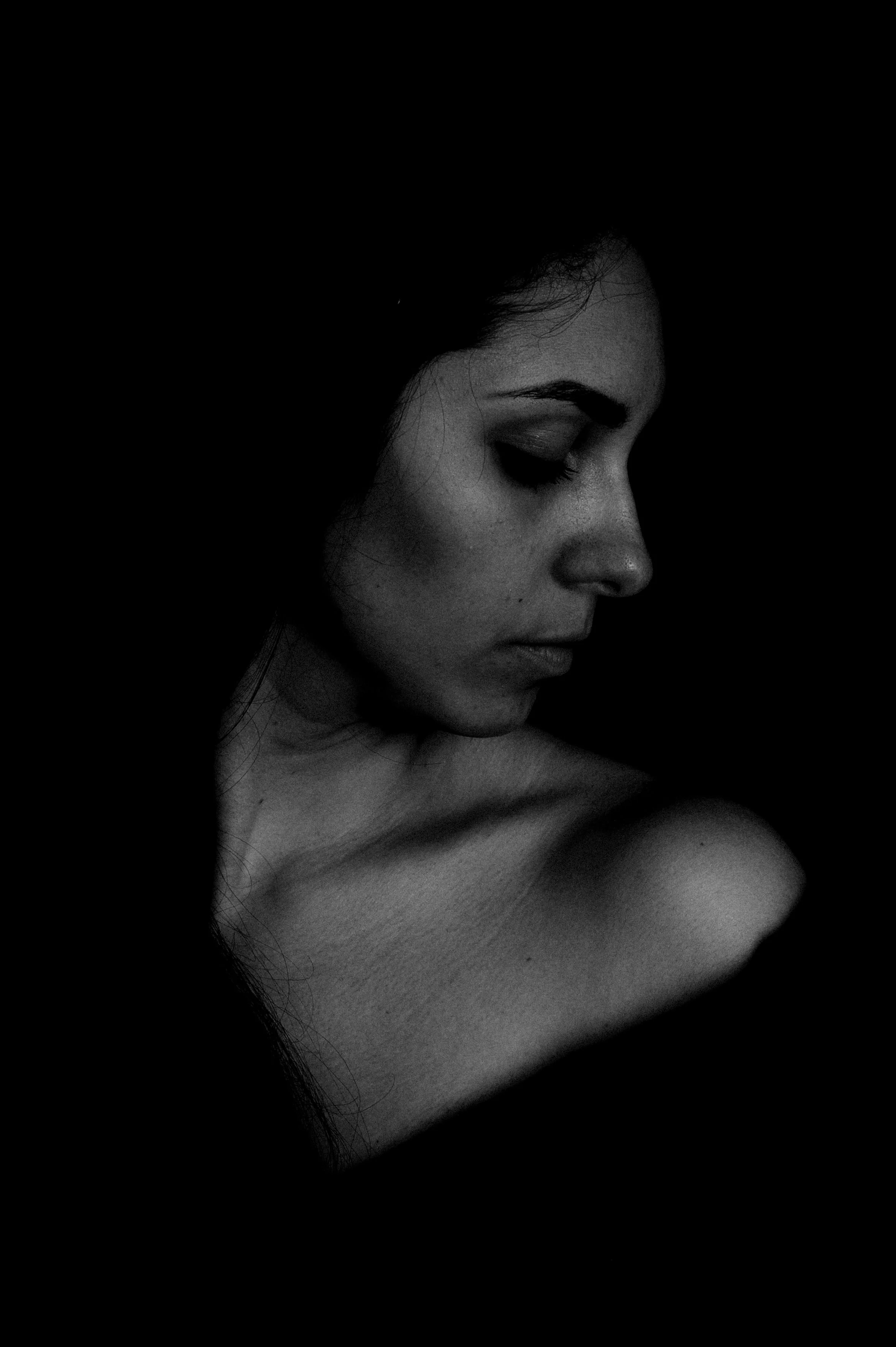 Portrait en noir et blanc d'une femme de profil regardant vers le bas, avec les épaules dénudées.
