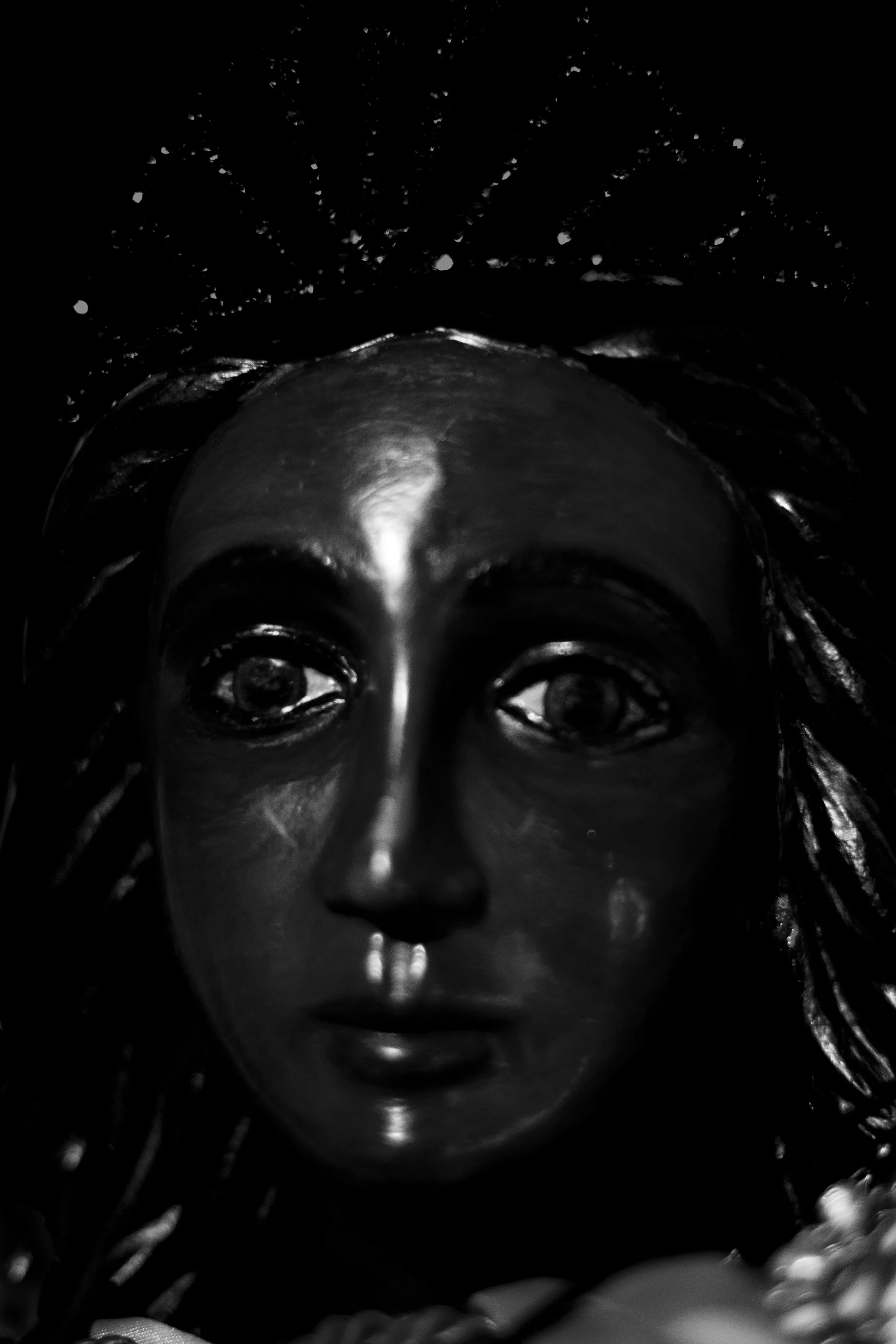 Close-up d'une statue de Vierge Marie en noir et blanc, avec un fond sombre et une expression douce.