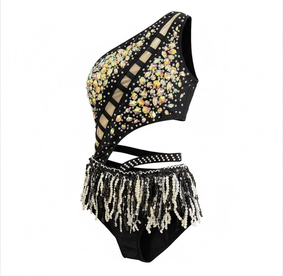 A black one-piece swimsuit with colorful rhinestones and pearl embellishments, featuring cutouts and fringe details.
