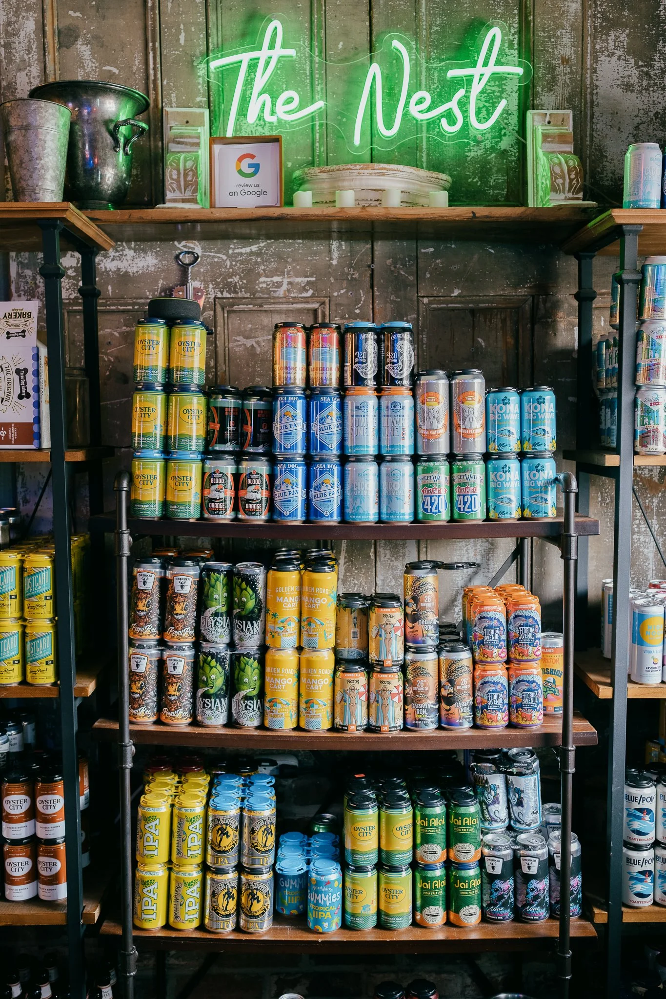 Display of canned beverages in a store, with a green neon sign above reading 'The Nest'.