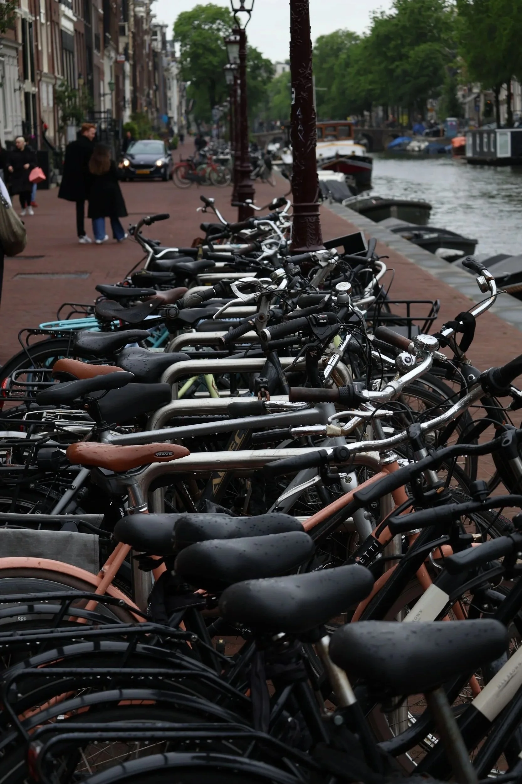 Low-angle close-up of densely packed bicycle saddles and handlebars parked along an Amsterdam canal. Brown leather and black saddles dominate the foreground in sharp diagonal perspective.
