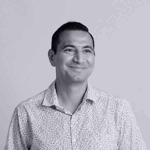 Black and white portrait of a man with slicked-back hair, wearing a patterned button-up shirt, smiling slightly, against a plain background.