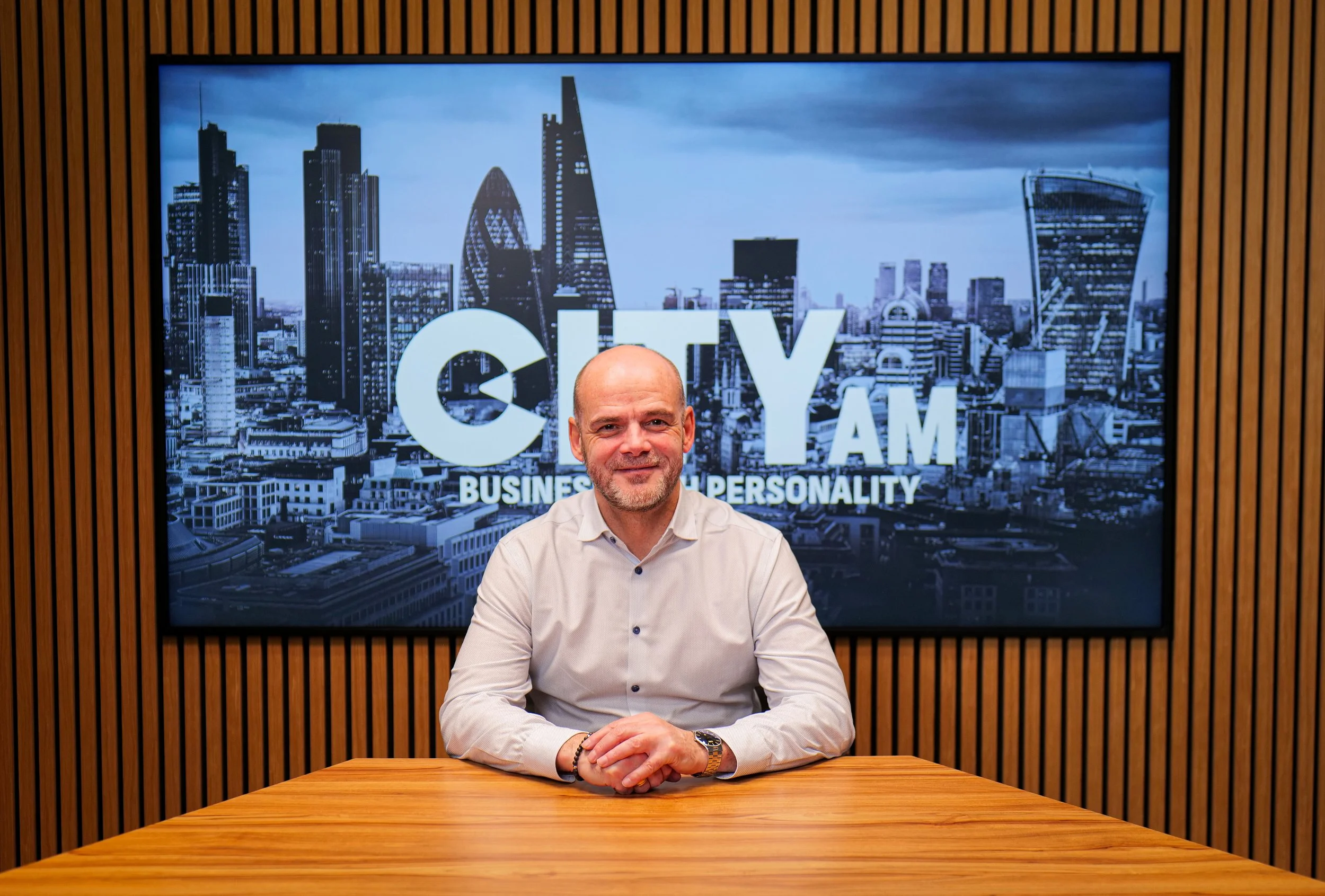 A black and white portrait of a middle-aged man with short hair, a beard, and a mustache, wearing a collared shirt and a zip-up jacket, standing against a plain white background.
