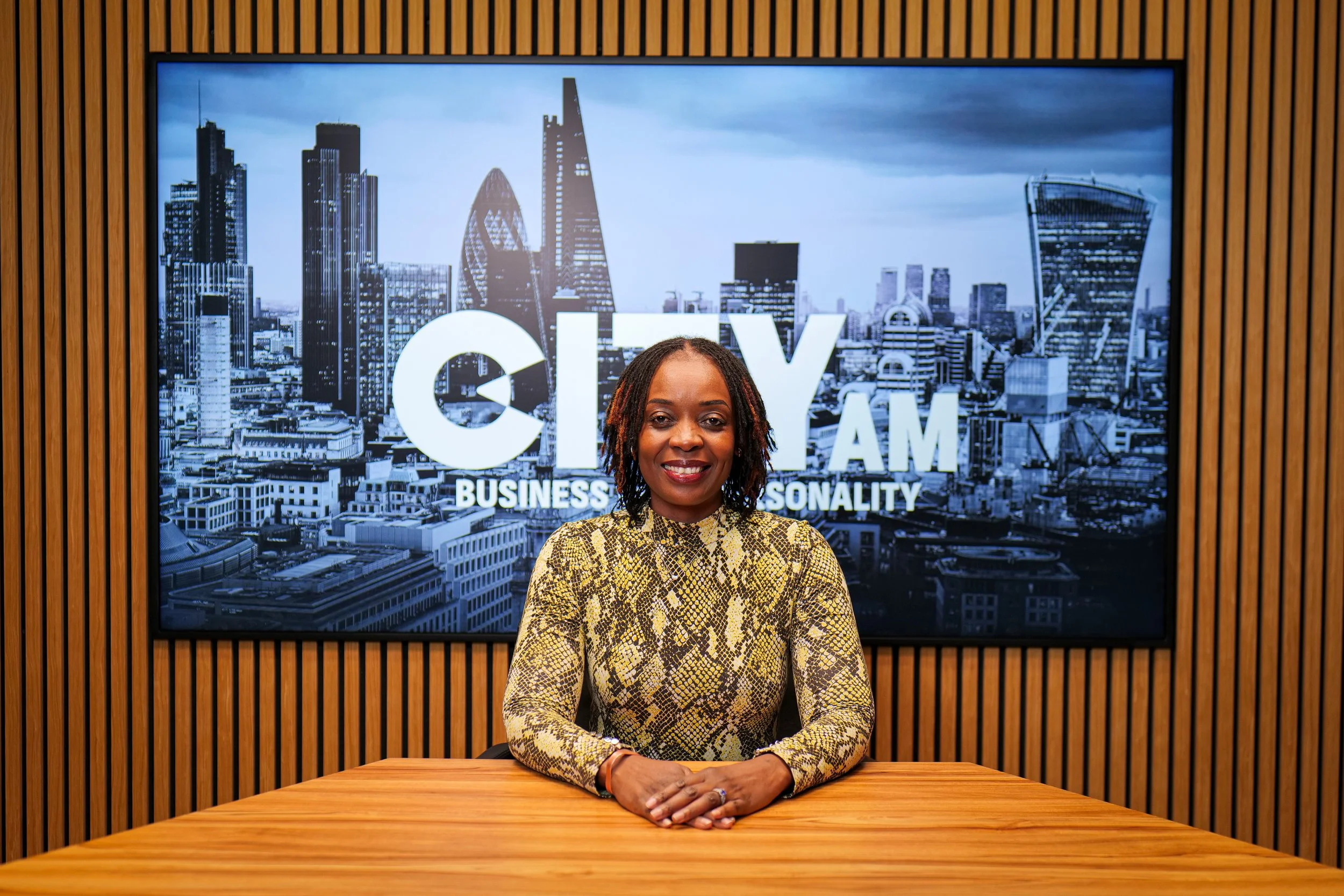Black woman with curly hair smiling, wearing a striped collared shirt, in black and white.