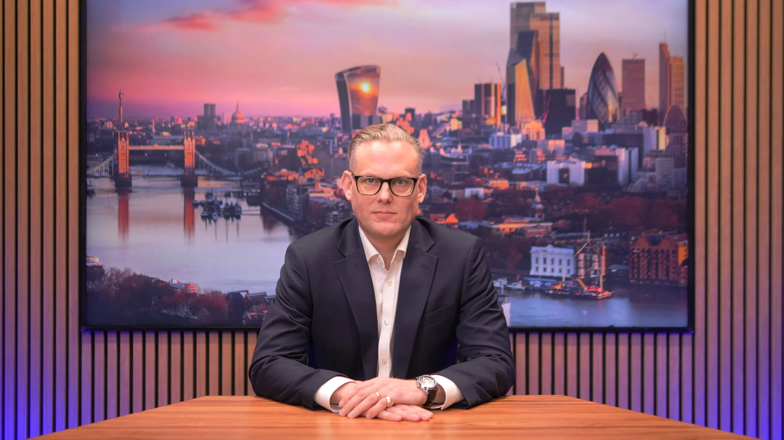 Black and white portrait of a man in a suit and tie, wearing glasses, smiling, against a plain light background.