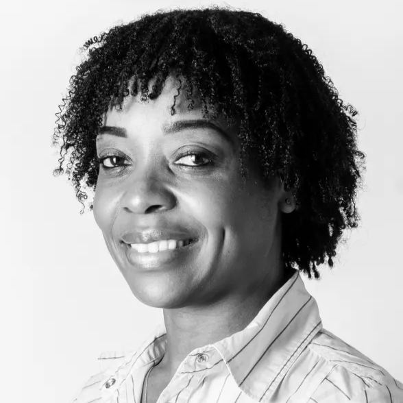 Black woman with curly hair smiling, wearing a striped collared shirt, in black and white.