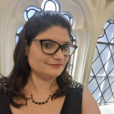 Close-up of a woman with dark hair and glasses inside a building with stained glass windows