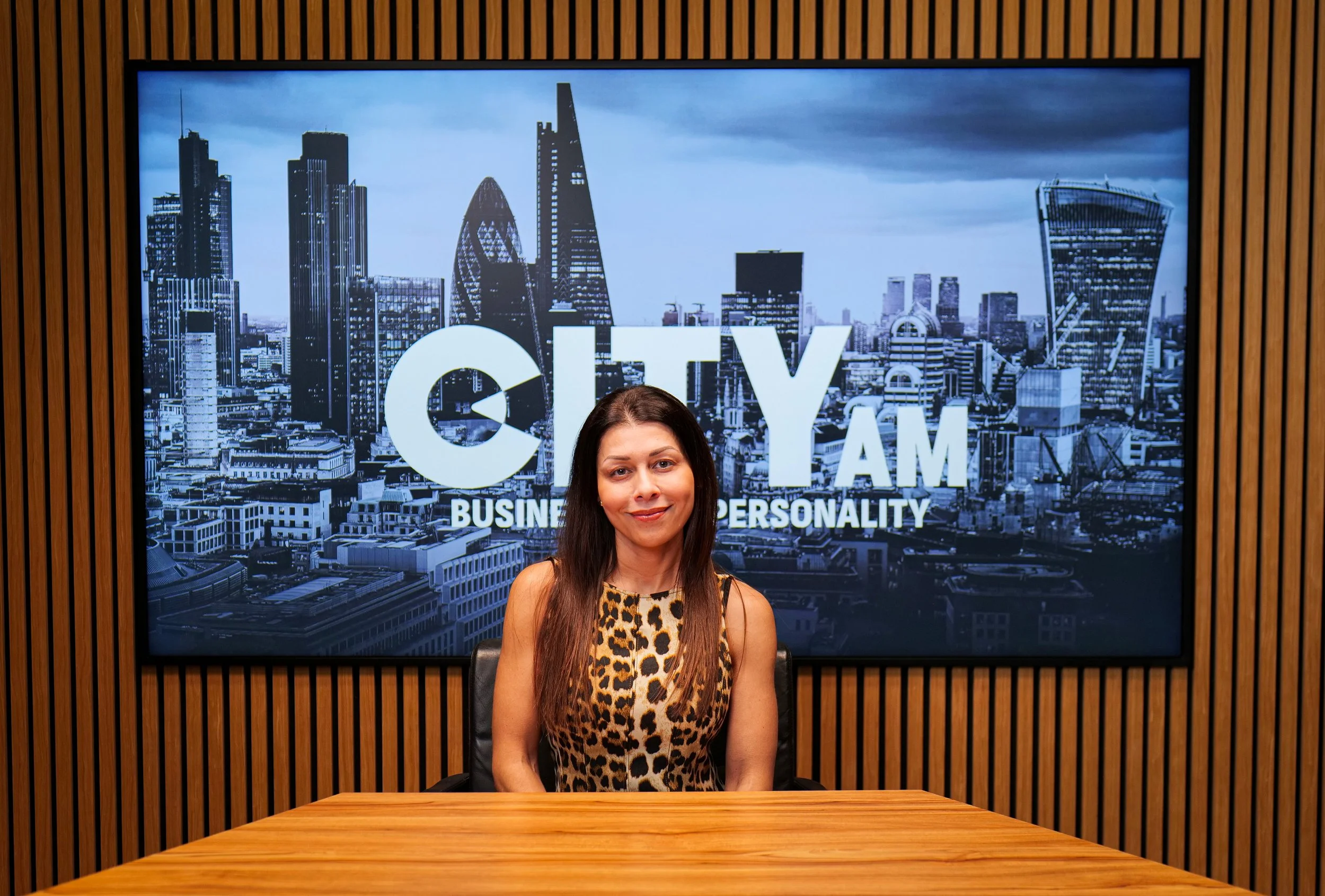 Black and white photo of a smiling woman with shoulder-length dark hair, wearing a dark top, standing against a textured wall.