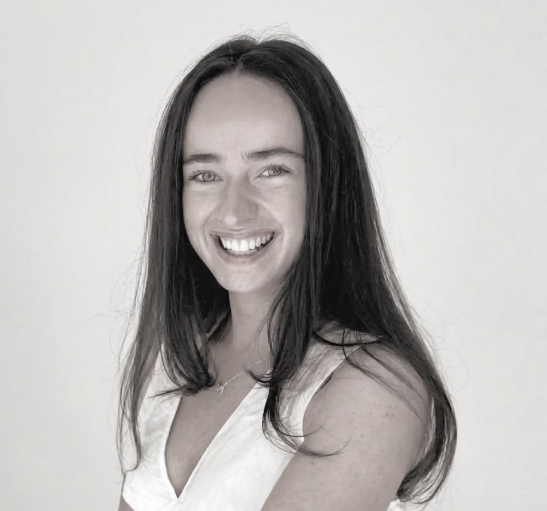 Black and white portrait of a man in a suit and tie, wearing glasses, smiling, against a plain light background.