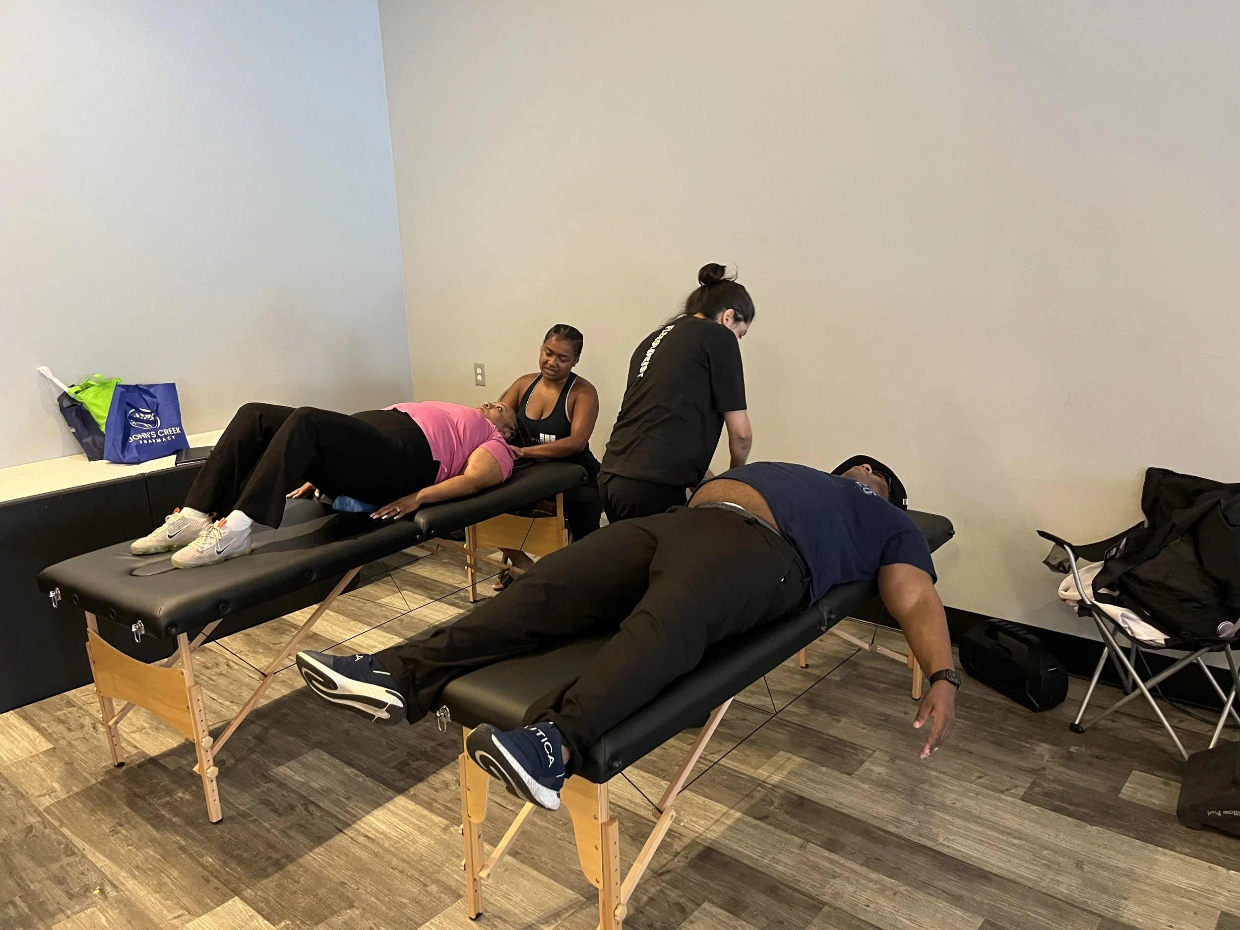 People lying on massage tables receiving therapy in a room with a gray wall.