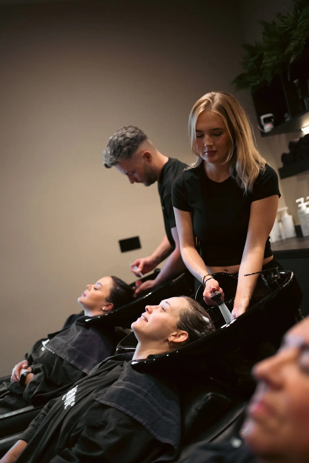 Women getting hair washed at salon with clients reclining in chairs and hairdressers washing their hair.