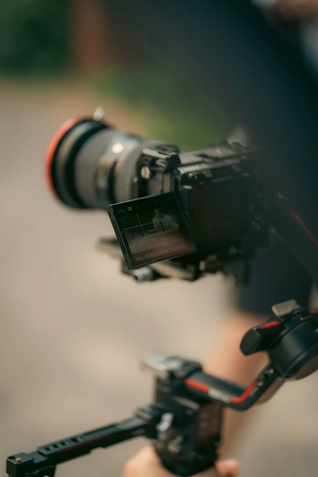 A camera mounted on a stabilizer rig, with a flip-out screen displaying a preview of the shot, set outdoors with blurred background.