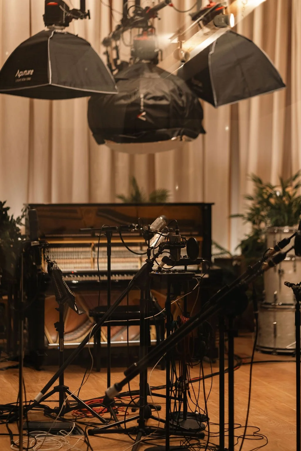 Recording studio with microphone setup, grand piano, and large black umbrella lights in a warm-lit room.