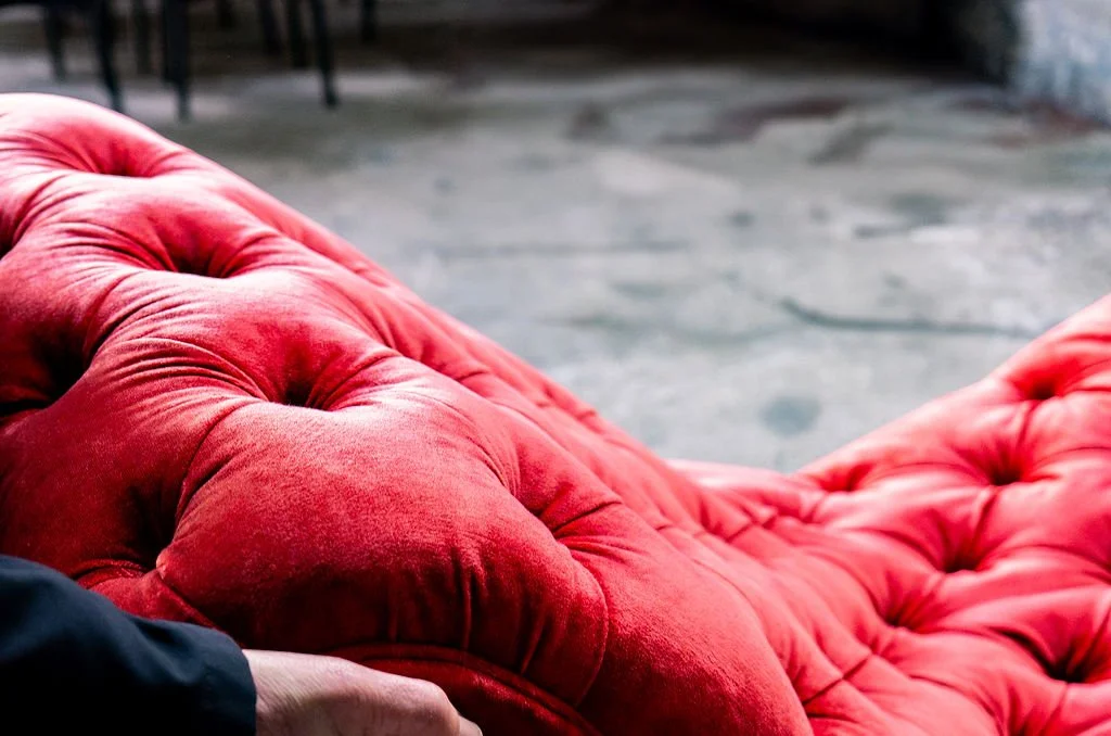 Close-up of a red velvet tufted chair with a dark background.