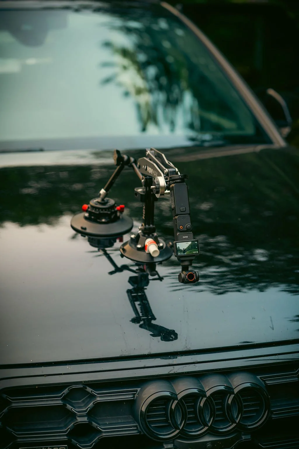 Camera mounted on a suction cup tripod on the hood of a black car, with the reflection of trees and sky on the hood.