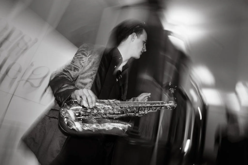 A man holding a saxophone in a blurred, black-and-white photo.