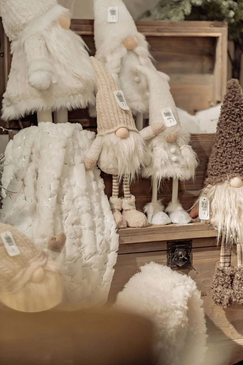 Display of plush gnome Christmas ornaments with hats and beards in white, beige, and brown on wooden shelves.