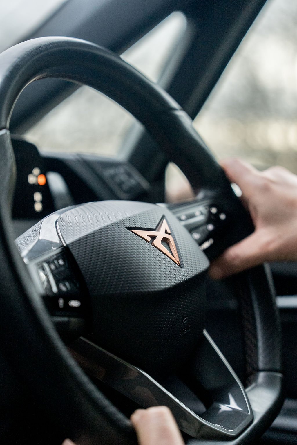 Close-up of a person gripping the steering wheel inside a car with a modern dashboard, focusing on a logo with a star symbol on the steering wheel.