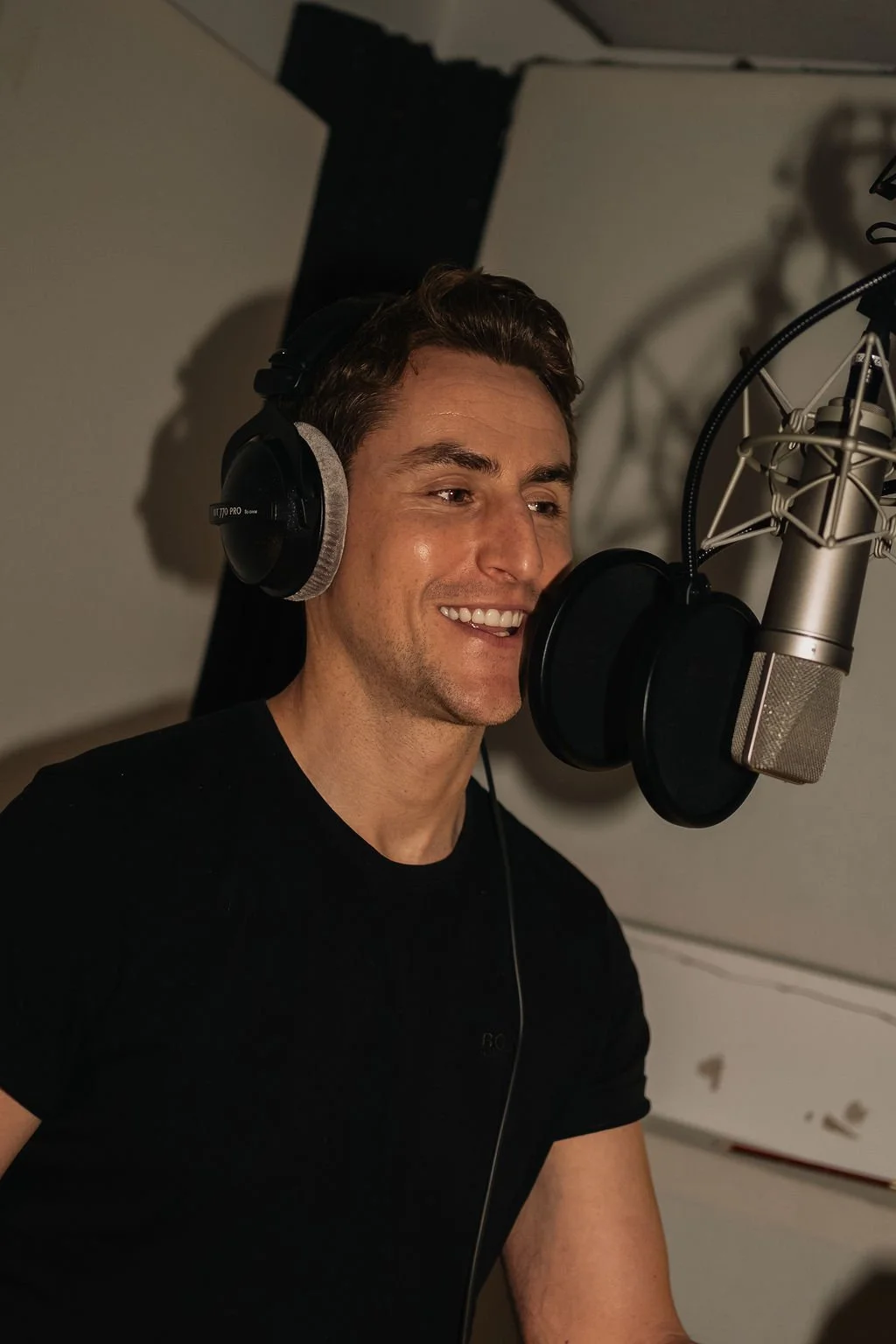 A man recording vocals in a sound studio with headphones and a large professional microphone.