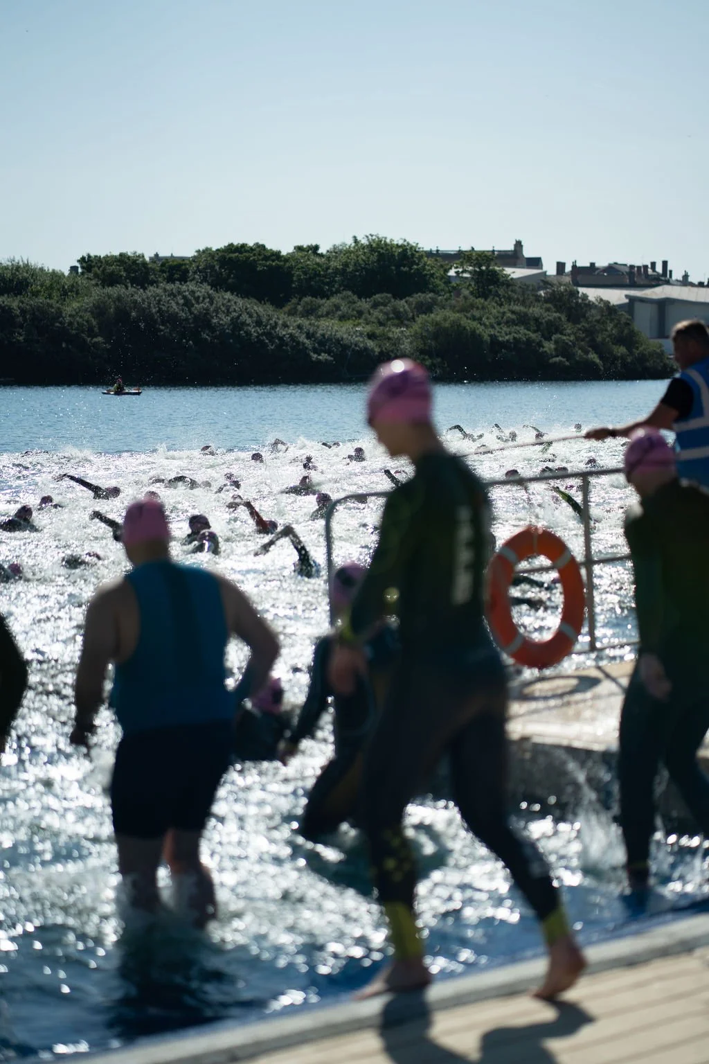 Swimmers in a race at an outdoor triathlon or swimming competition, with some participants exiting the water and others still swimming.