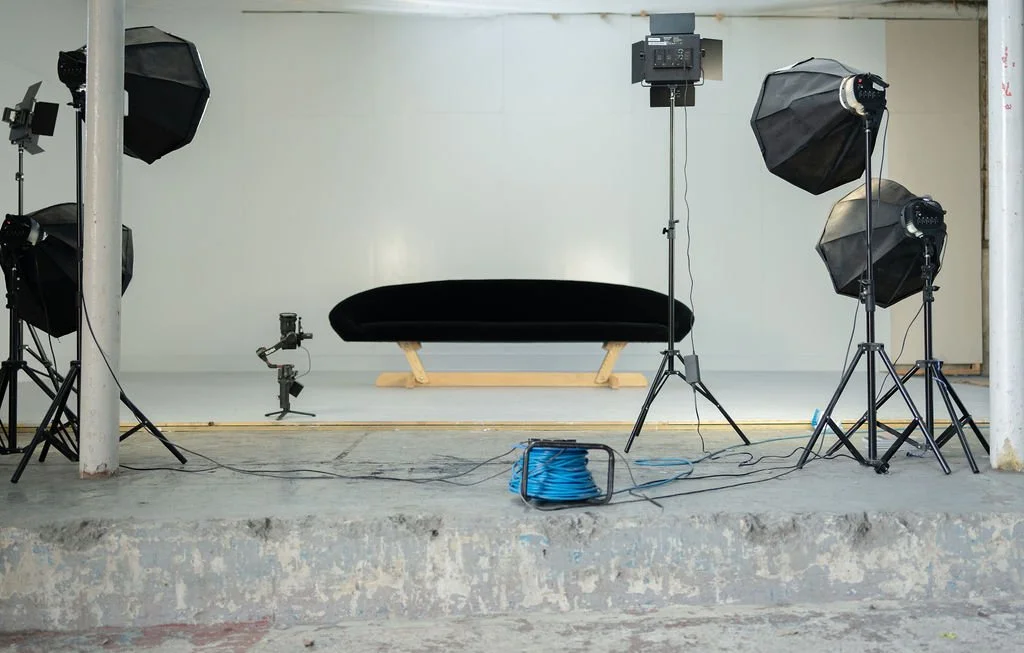 Photography studio setup with lighting equipment, a black bench, and a white backdrop.