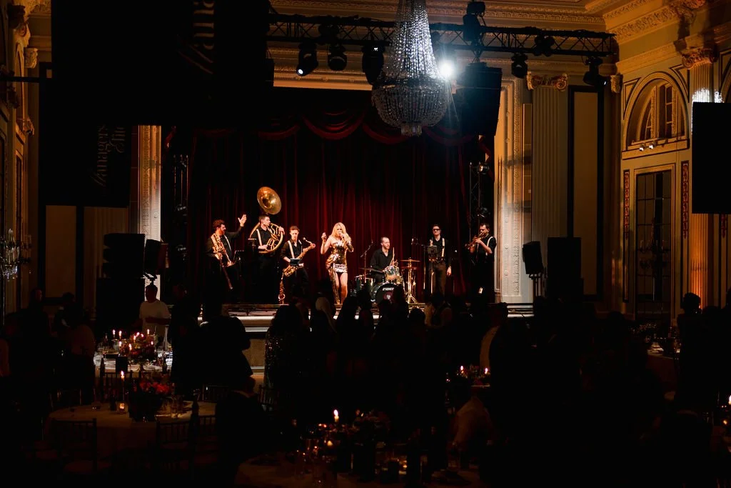 Live jazz band performing on stage at an elegant event venue with audience seated at candlelit tables.