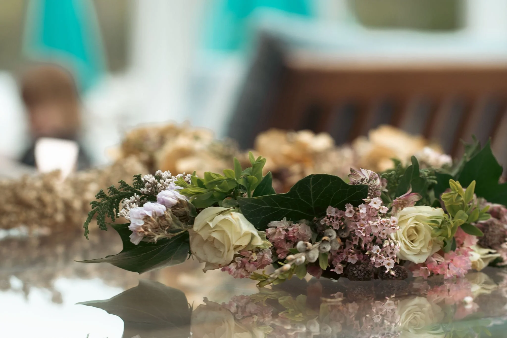 A floral arrangement with white roses, pink flowers, green leaves, and other small flowers, placed on a reflective surface.