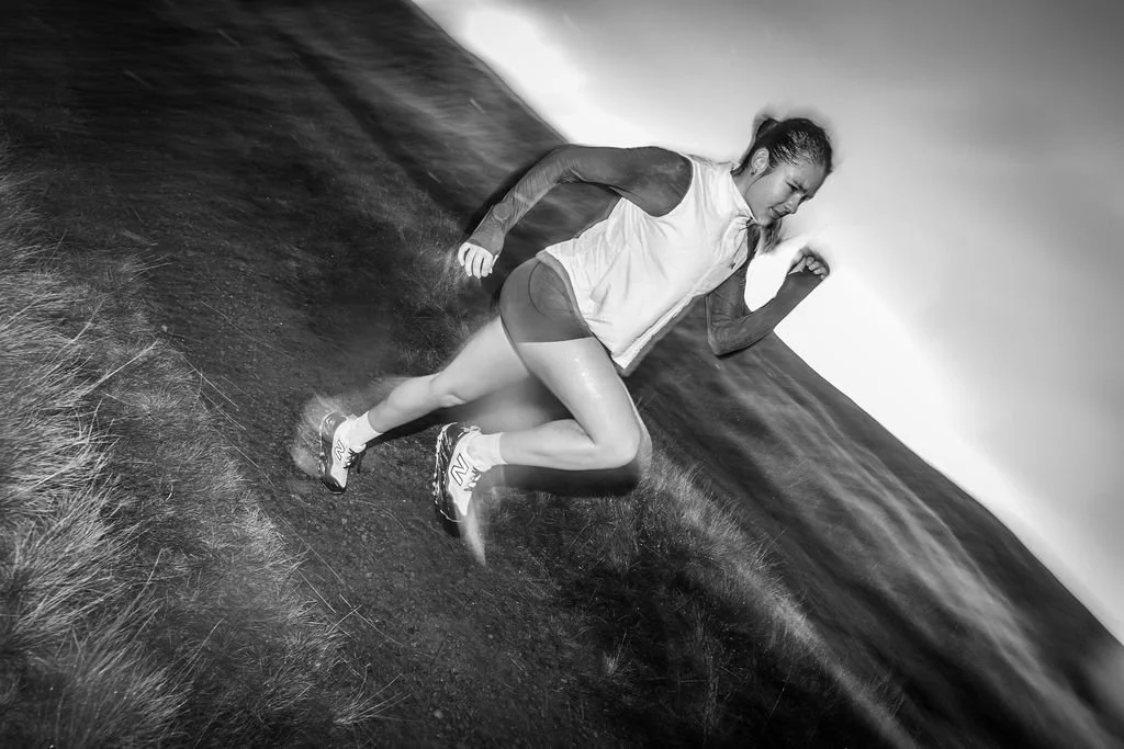 A woman running outdoors on a grassy trail in black and white.