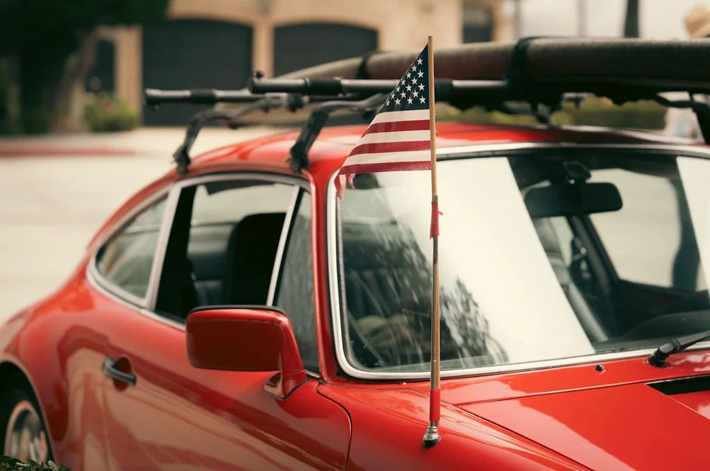 Close-up of a red vintage car with a small American flag attached to the front window.