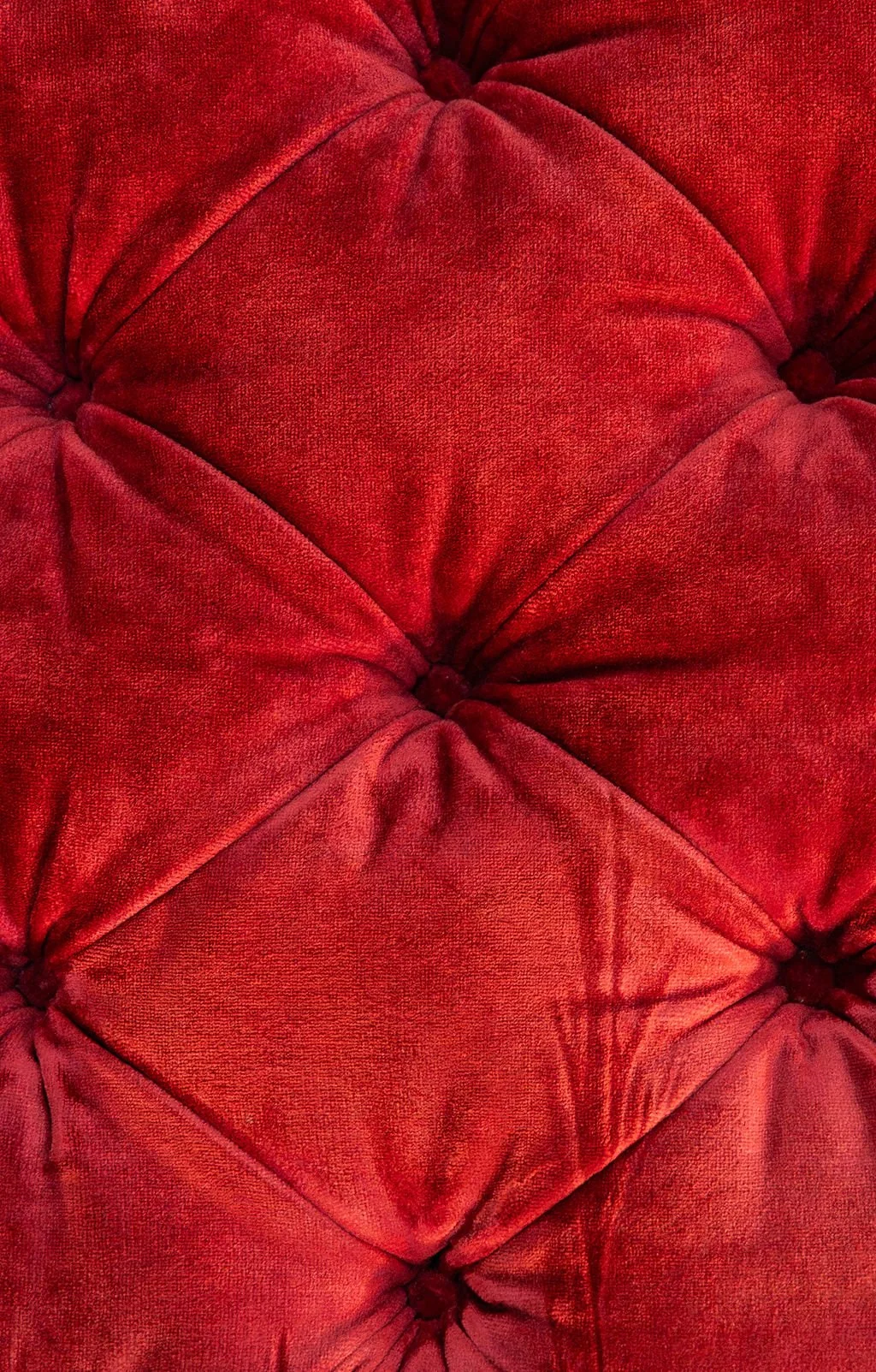 Close-up view of red velvet tufted upholstery with button-tufted detailing.