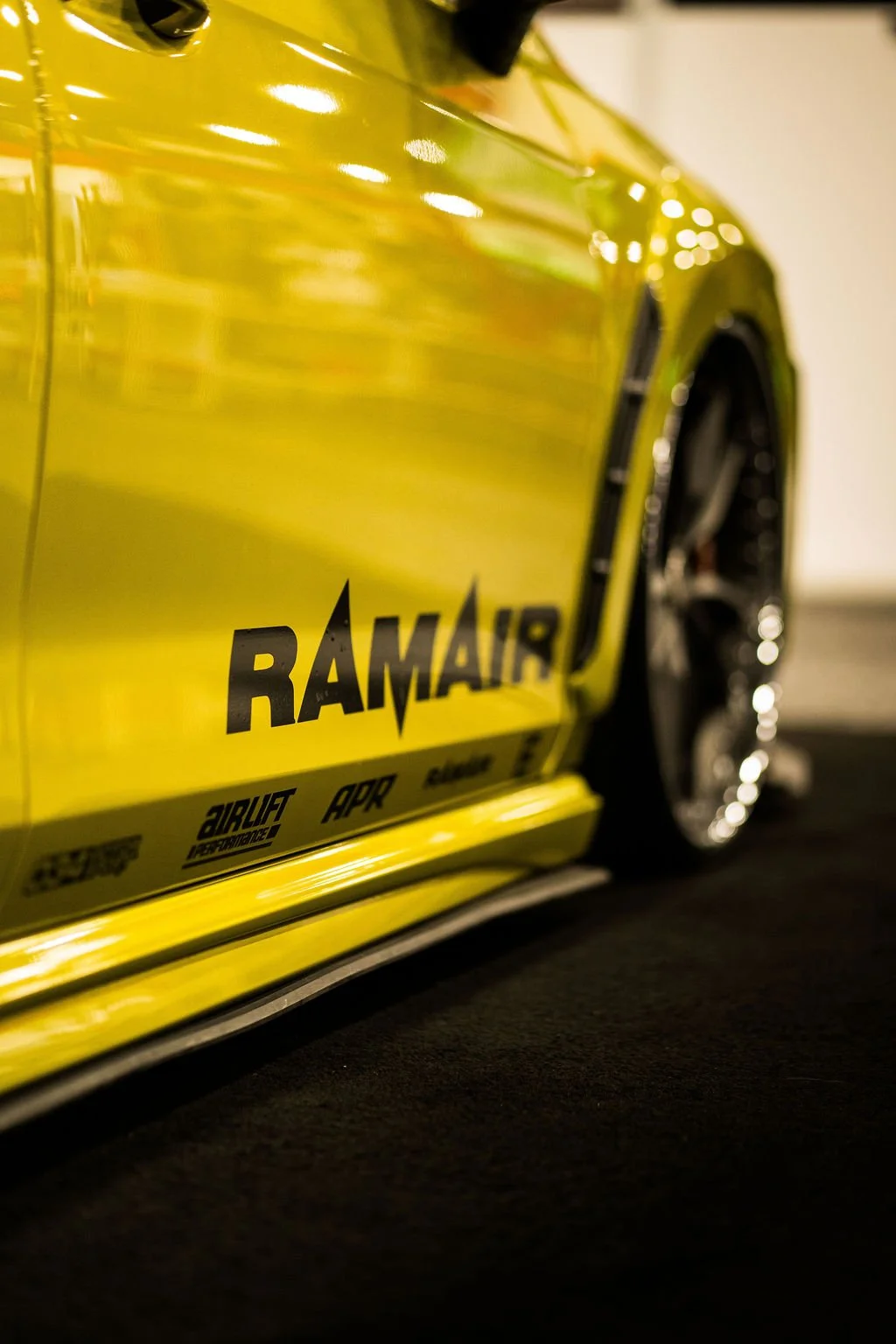 Close-up of a yellow car with black wheels, featuring the RAMAIR logo and various sponsor decals.