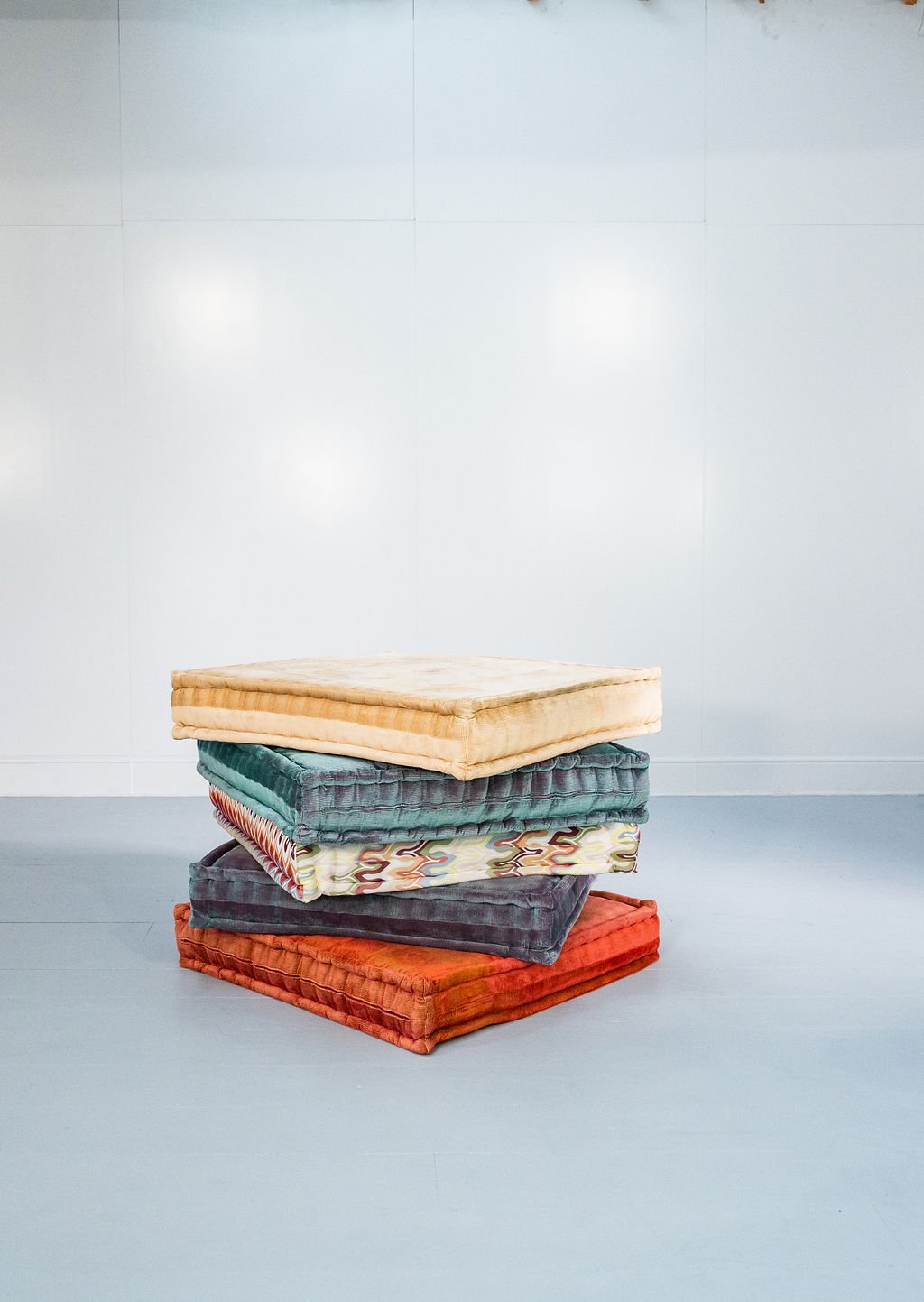 Stack of five, large colourful, folded cushions.