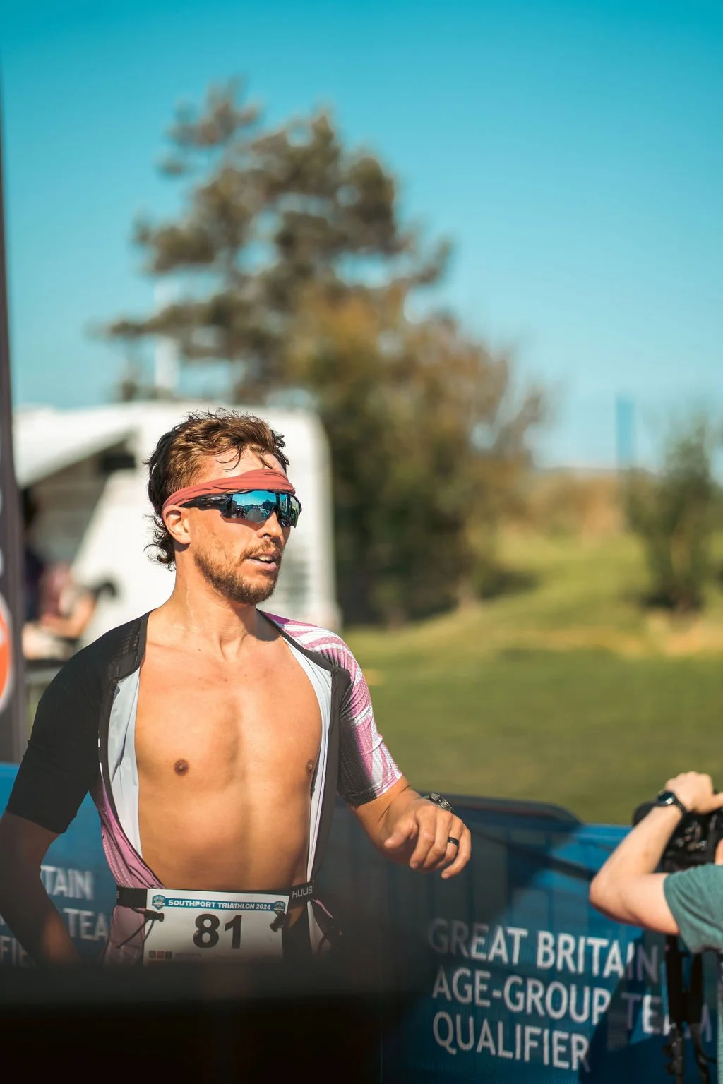 Male triathlete wearing sunglasses, a headband, and a race bib number 81, running outdoors during a triathlon event.