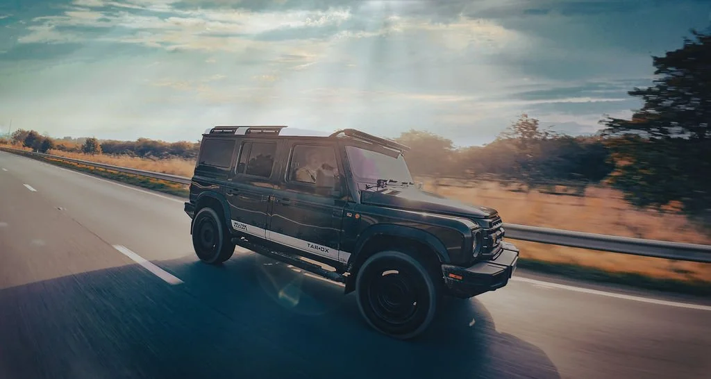 Black SUV driving on a highway with a sunset sky and trees in the background.