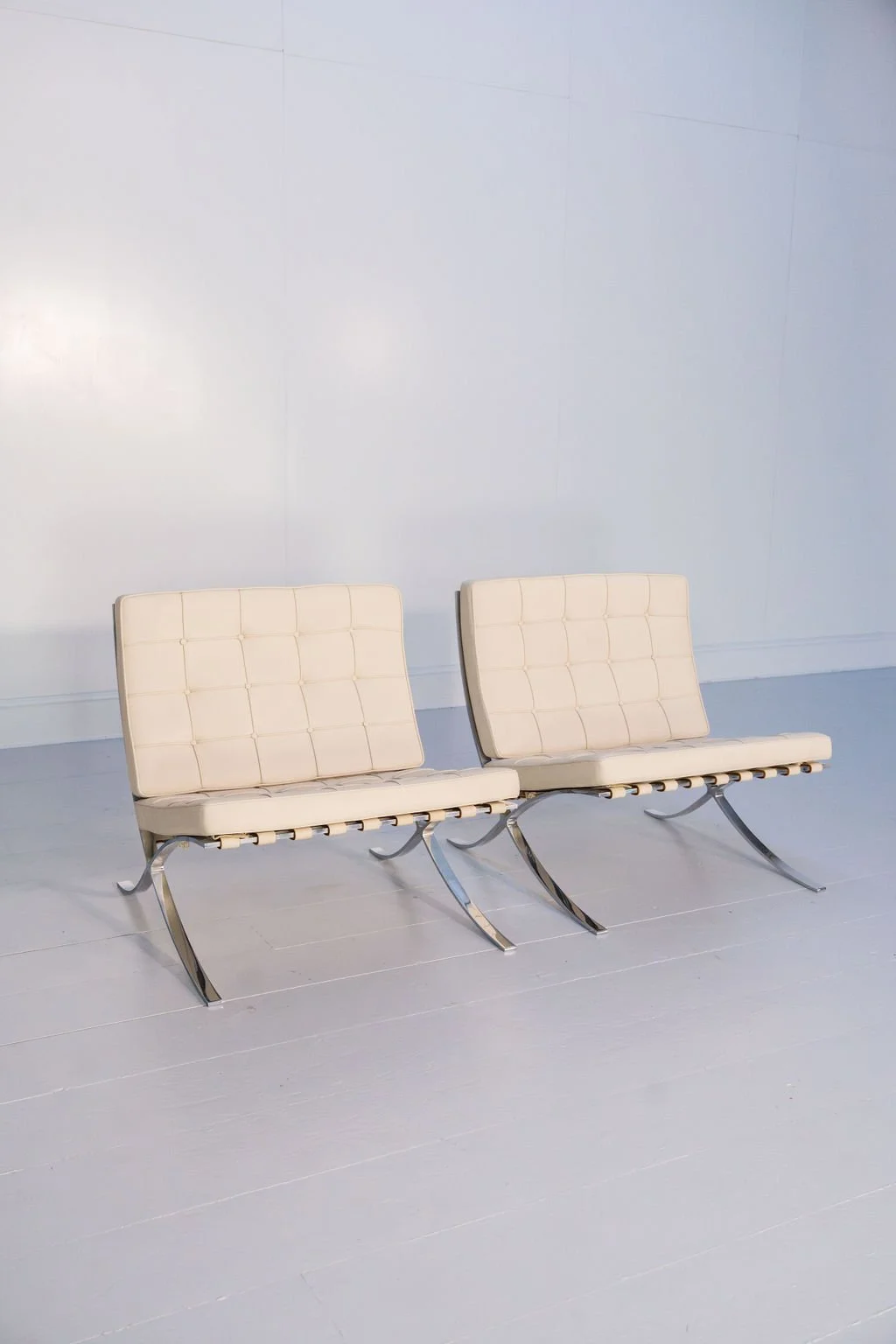 Two cream-colored modern waiting chairs with metal legs in a minimalist room with white walls and flooring.