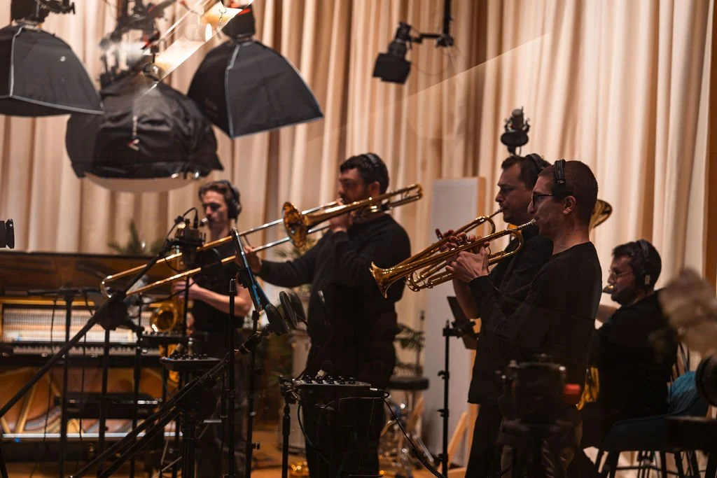 A group of musicians playing brass instruments in a recording studio with professional lighting and sound equipment.