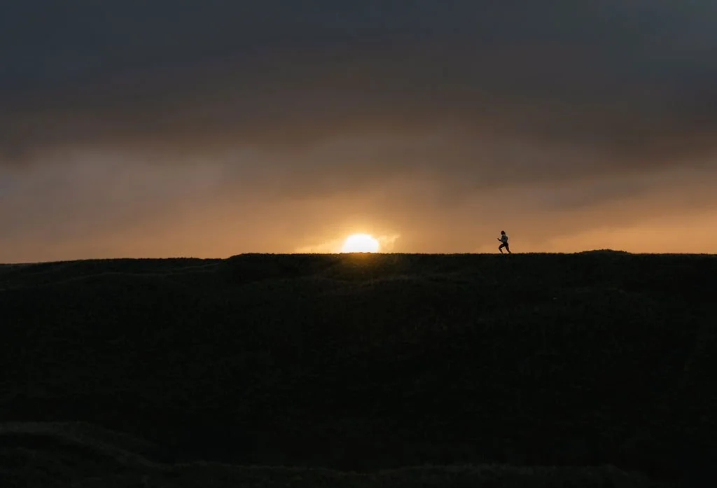 A person jogging on a hill at sunrise or sunset with a partly cloudy sky.