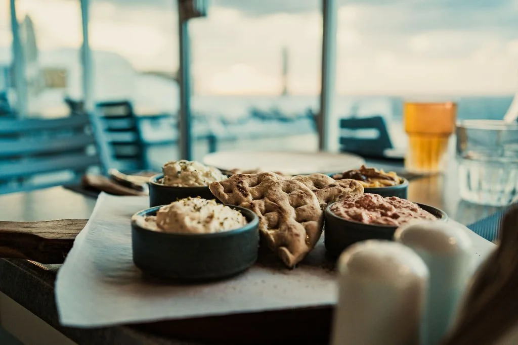 Assorted breads and dips, woth a pool and the ocean in the background on a Greek island.