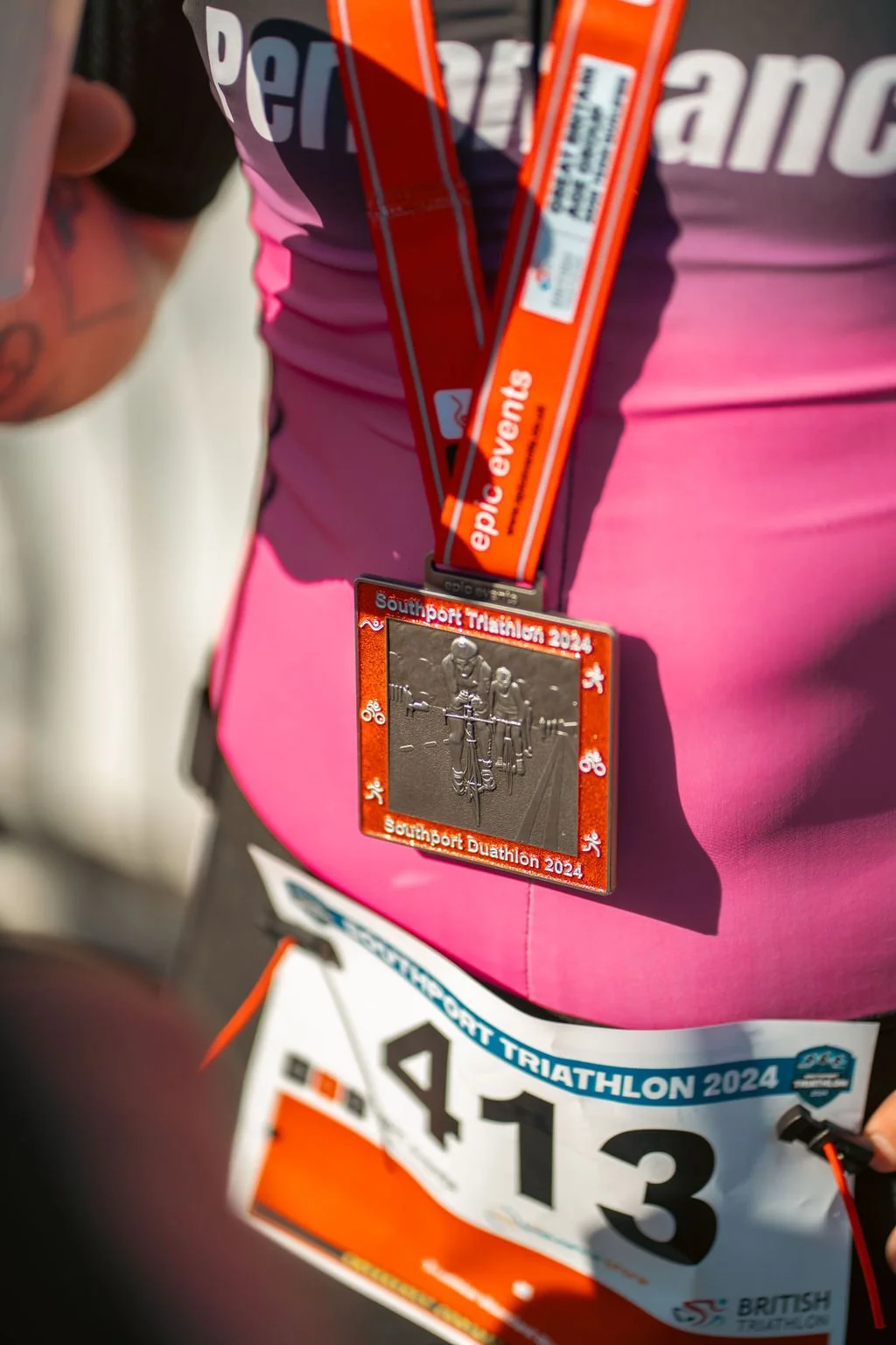 A participant at the Southport Triathlon 2024 wearing a bib number 413, pink athletic clothing, and a medal around their neck.