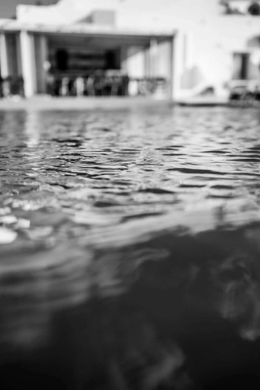 Close-up of water ripples with a blurred building or structure in the background in black and white.