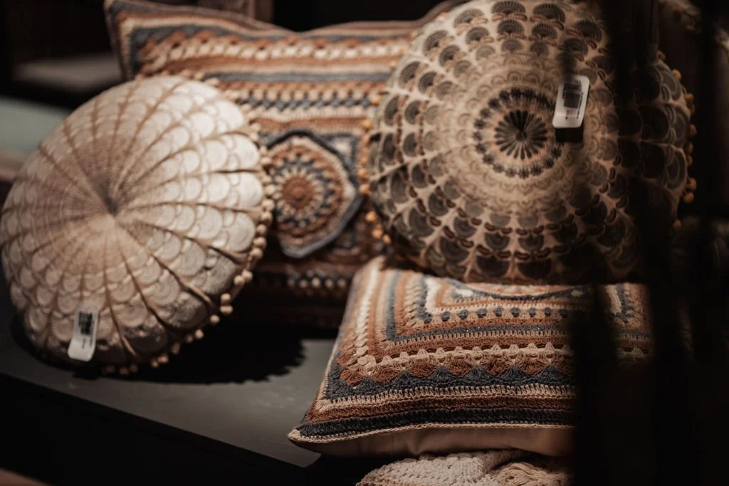 Decorative pillows with intricate patterns and textures, some with tags, placed on a dark surface.