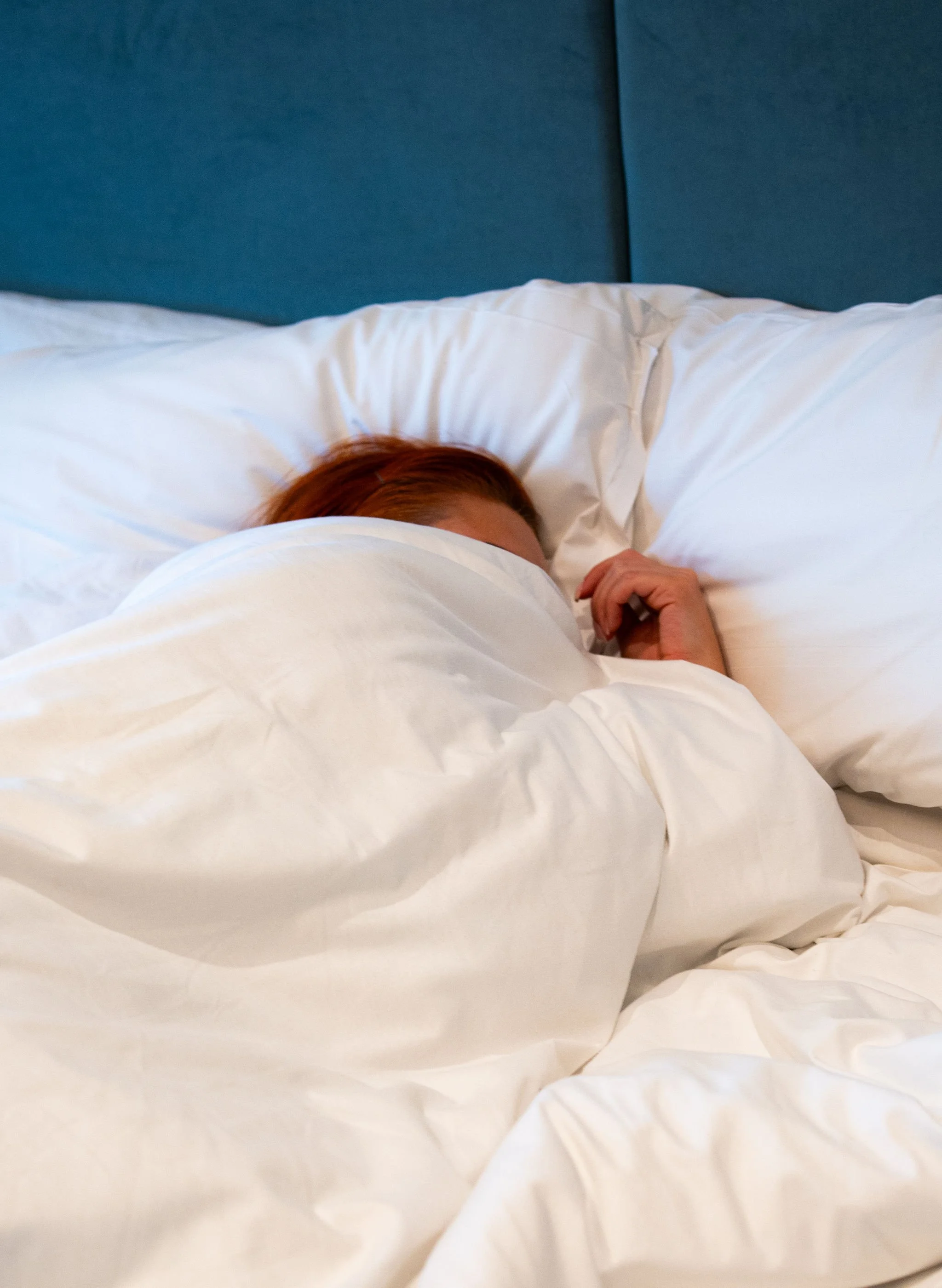 Person with reddish hair sleeping under white sheets in bed.