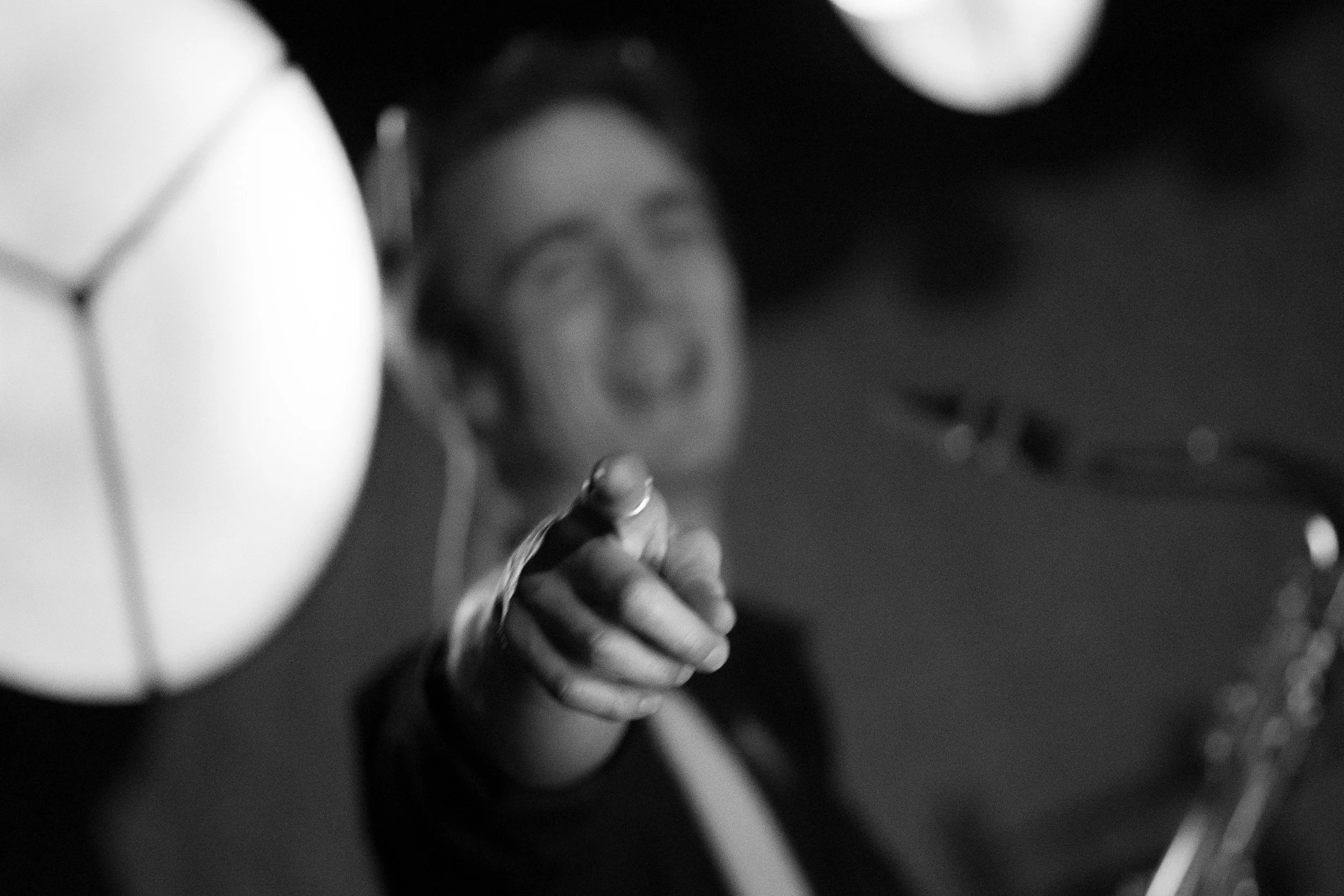 A person smiling and pointing at the camera, with a lamp in the foreground, in a black and white photo.