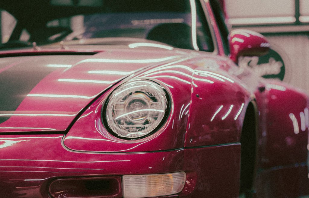 Close-up of a pink porsche RWB sports car with a rounded headlight and reflective surface.
