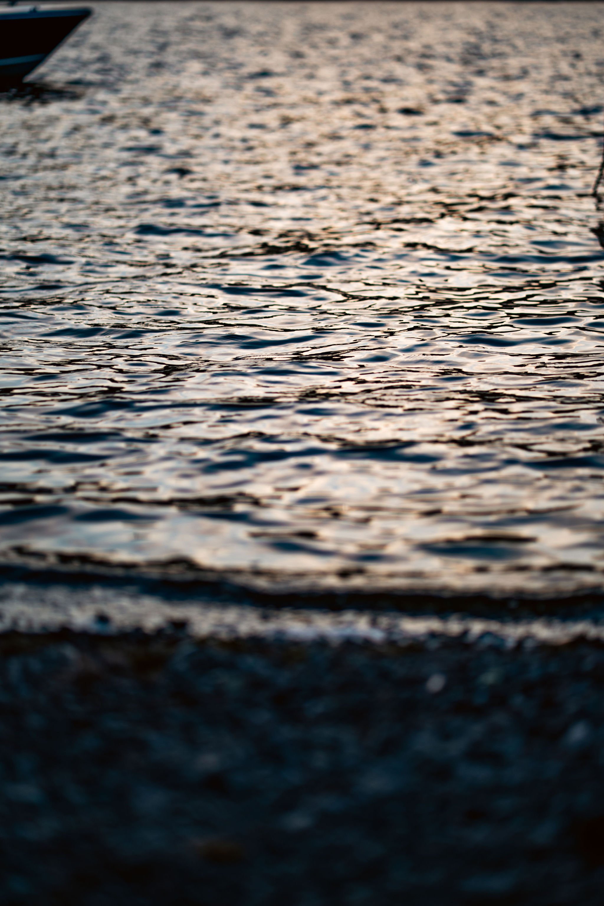 Close-up of rippling water on a body of water, with the light reflecting off the surface during sunset.