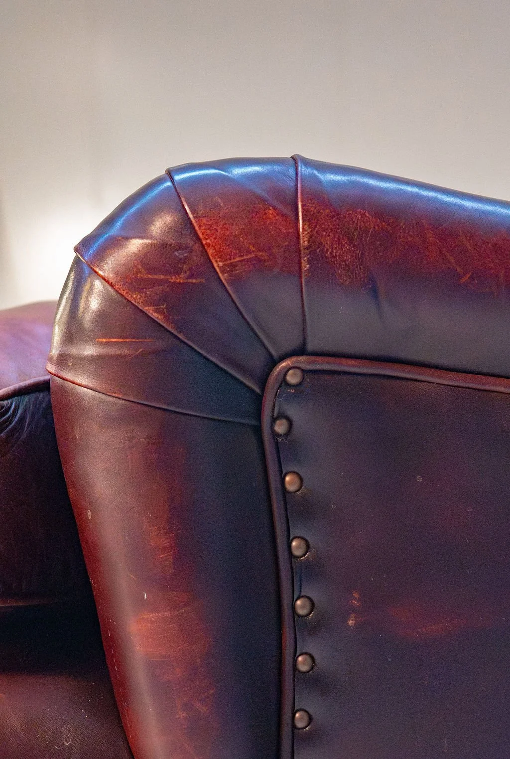 Close-up of a worn, dark brown leather armchair with nailhead trim on the backrest.