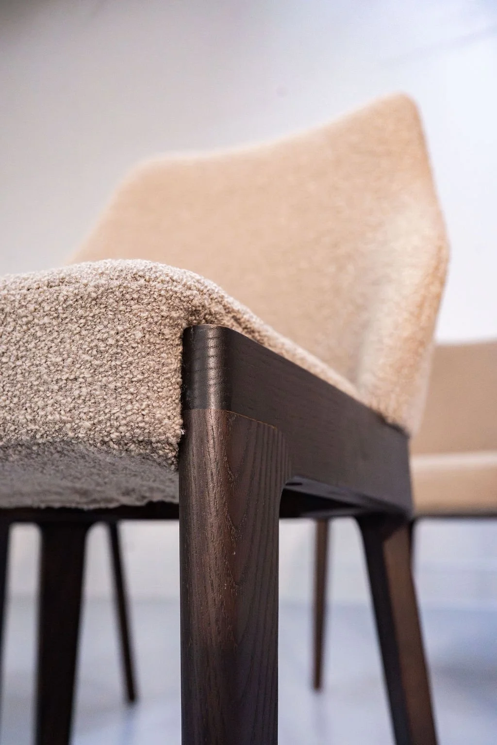 Close-up of a modern wooden dining table with a textured beige cushion and a beige upholstered chair in the background.