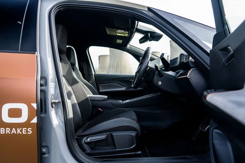 Interior of a modern vehicle showing the driver's seat, steering wheel, dashboard, and part of the passenger seat.